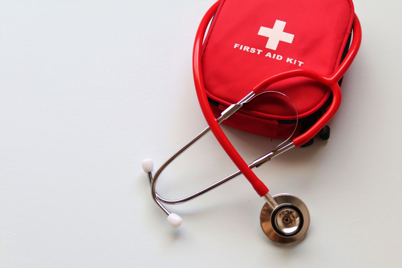 Une trousse de premiers secours rouge et un stéthoscope sur une surface claire.