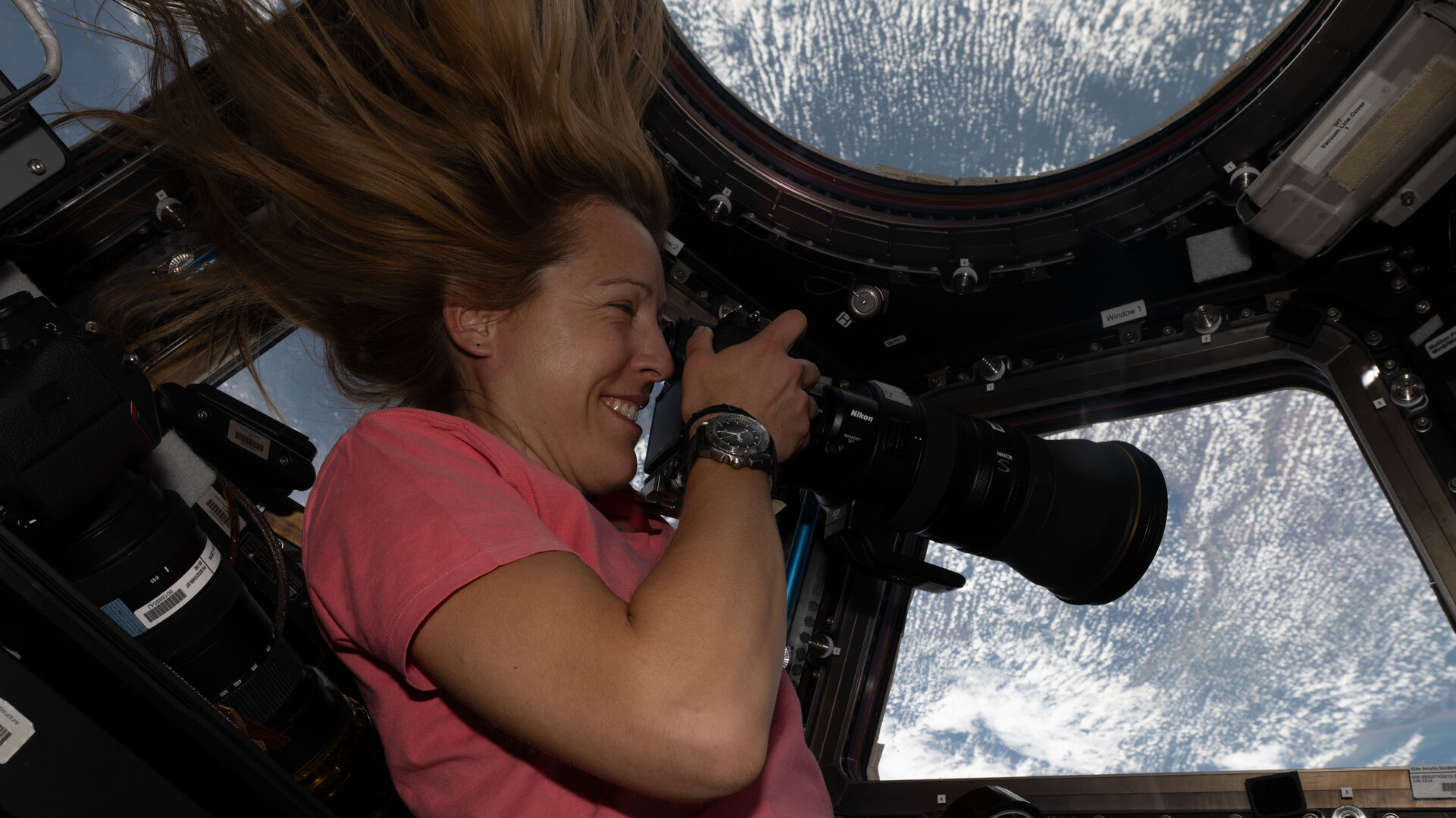 Sophie Adenot, les cheveux en apesanteur, tient un appareil photo dans la coupole de l’ISS, avec la Terre en arrière-plan.