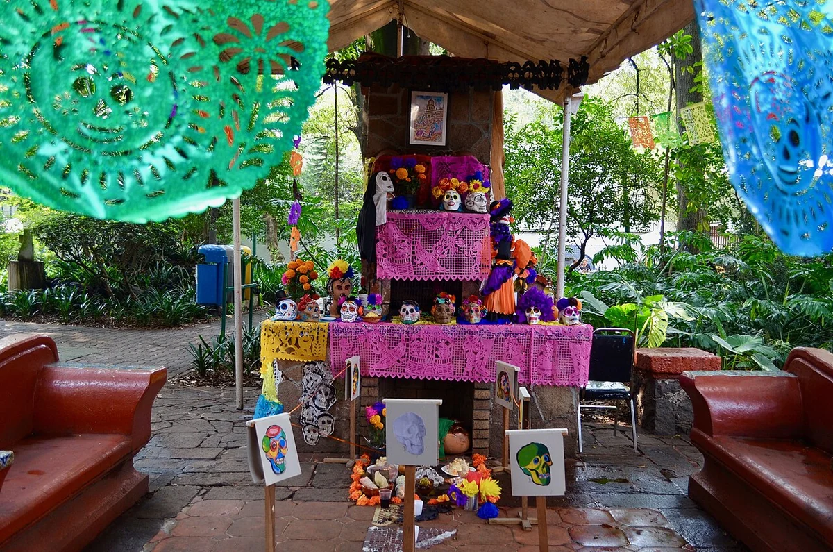 Fête des morts au Mexique : ofrenda à Coyoacán, fleurs orangées, crânes décorés et papier découpé rose.