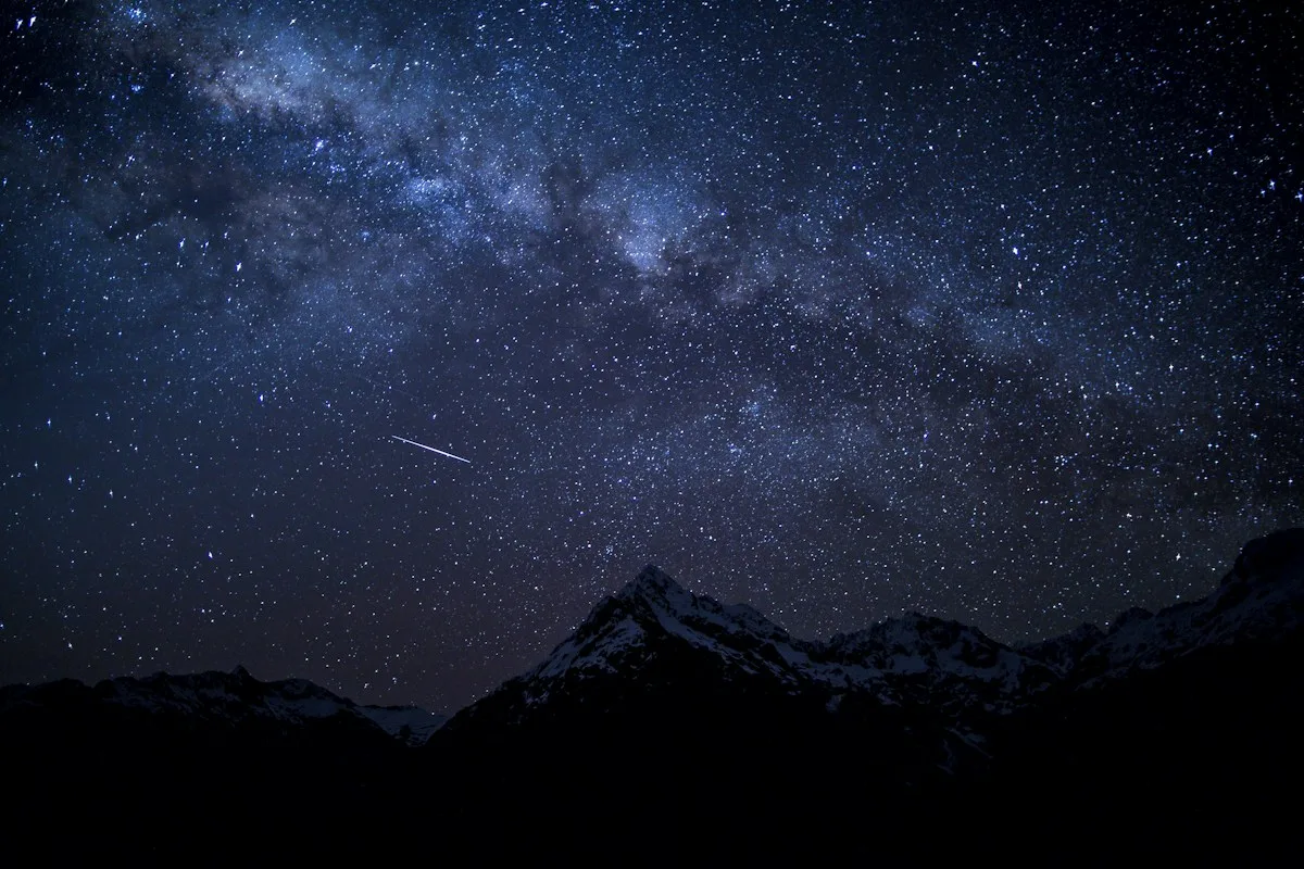 Un ciel rempli d’étoiles au-dessus de montagnes sombres.